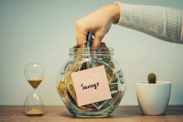 Photo female hand taking money from the glass jar with inscription savings toned image using saved up money from the bank