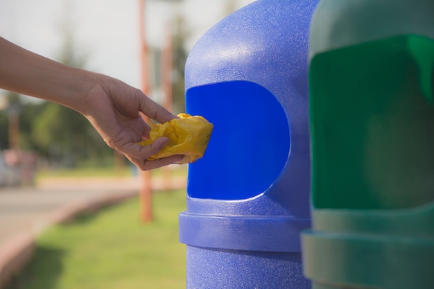 女性の手が青いプラスチックゴミ箱に黄色のプラスチックをぶら下げて投げた。