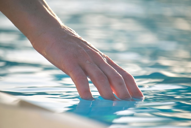 Female hand touching water of swimming pool in summer