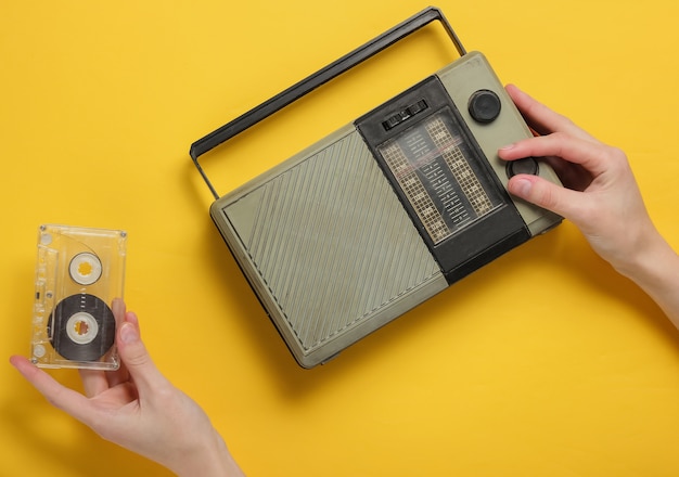 Photo female hand tunes retro radio receiver and holds audio cassette on yellow background