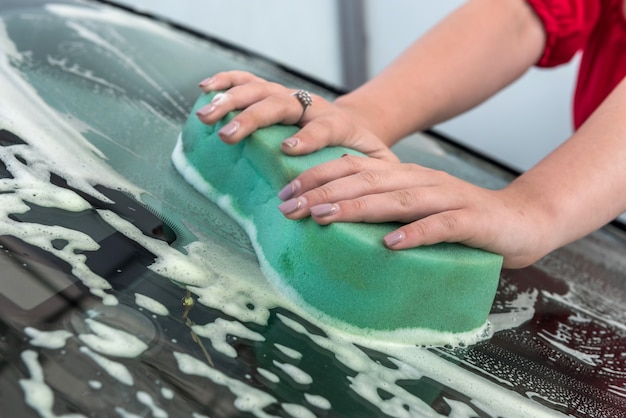 Женская рука, используя губку с мыльной пеной, чистит машину на автомойке