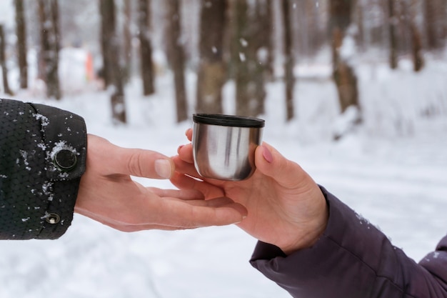 Female hand in a winter park passes a mug with a hot drink to friend