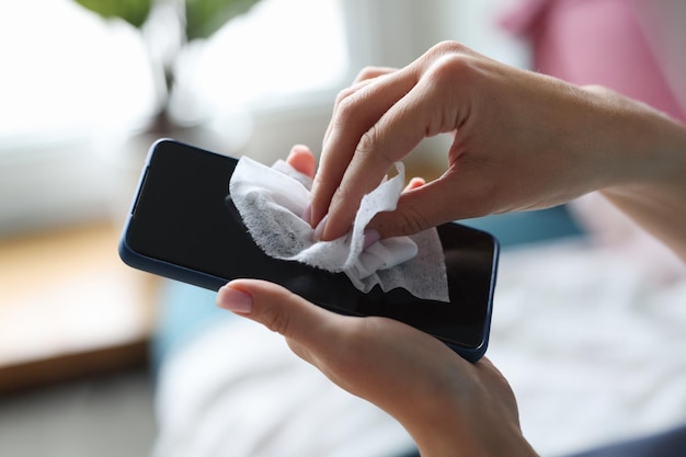 Female hand wipes smartphone with disinfectant napkin from bacteria