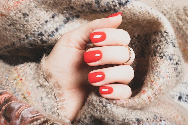 Female hand with bright red manicure on a background of brown woolen plaid