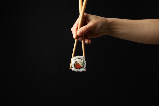 Female hand with chopsticks hold sushi roll on black surface.\
japanese food