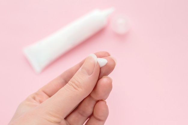 Female hand with a drop of cream on a finger. Tube of cream isolated on a pink background. Antibacterial acne cream for problem skin