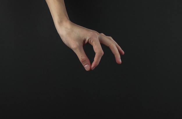Female hand with fingers holds something on black background.