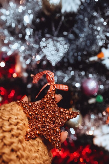 Photo female hand with french manicure holding a red toy heart against a background of christmas bokeh