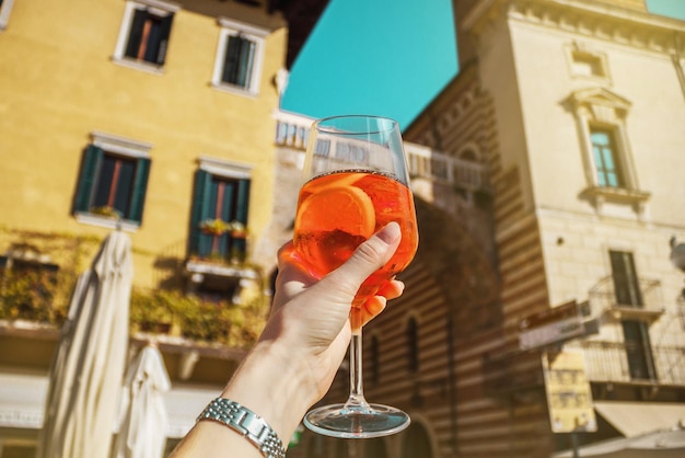 Photo female hand with glass of orange cocktail spritz near old buildings sunny day in verona italy