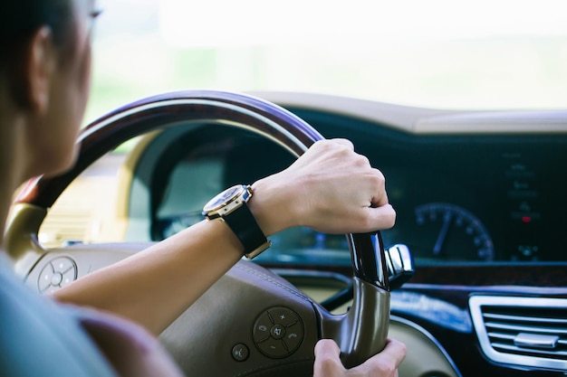 Mano femminile con orologio nero oro che tiene il volante in pelle in auto