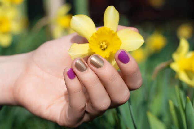 Photo female hand with gold and purple nail design holding blossom flower