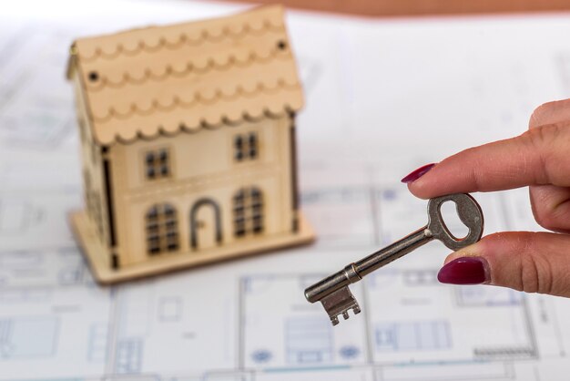 Female hand with key and toy house on plan