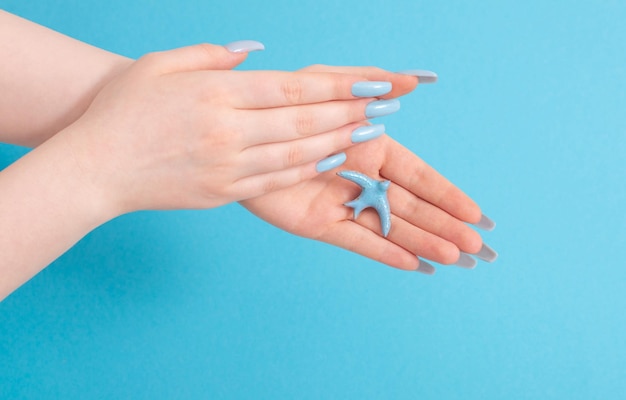 Female hand with manicure and ceramic bird on blue background