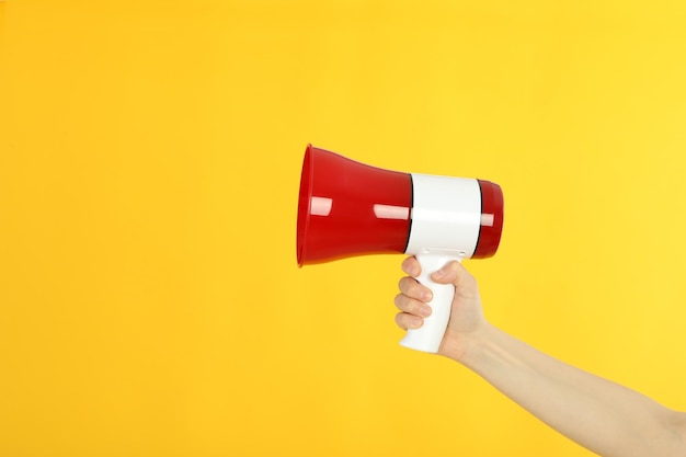 Female hand with megaphone on yellow background