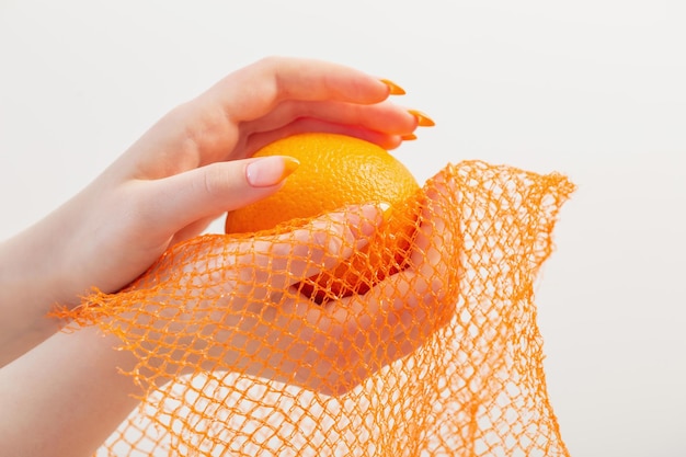 オレンジと合成ストリングバッグの女性の手