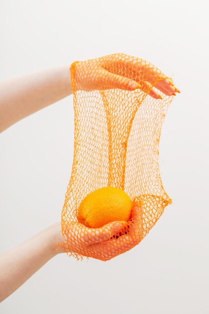 オレンジと合成ストリングバッグの女性の手