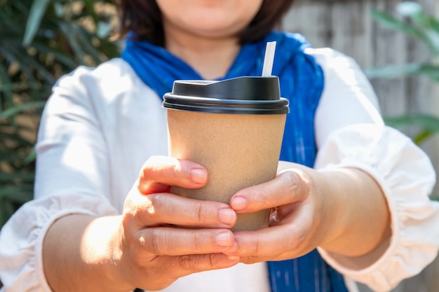 Mano femminile con un bicchiere di carta di caffè da asporto, tazze di caffè di carta nelle mani delle donne con una manicure perfetta