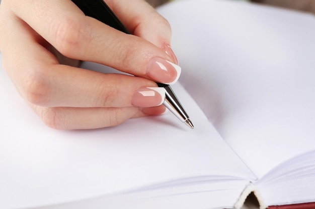 Female hand with pen writing on diary closeup