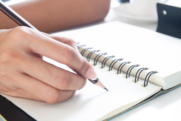 Foto mano femminile con scrittura della matita sul taccuino, fine sul colpo