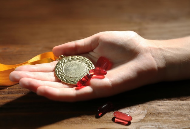 Фото Женская рука с таблетками и медалью допинг в спортивной концепции