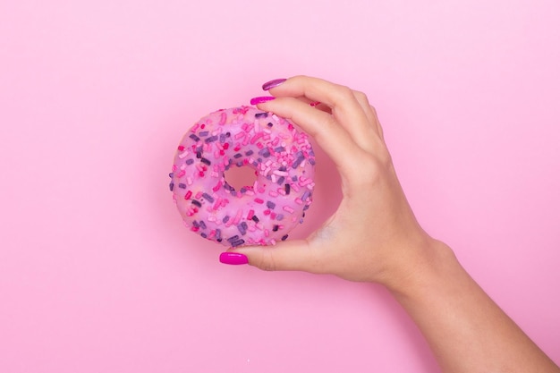 Mano femminile con unghie rosa per manicure che tengono ciambella alla fragola