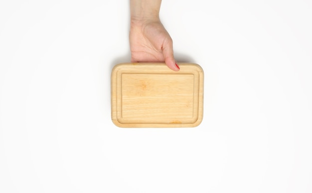Female hand with red manicure holds empty wooden rectangular kitchen chopping board on white background