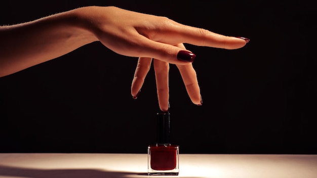 Mano femminile con manicure rossa e bottiglia di smalto