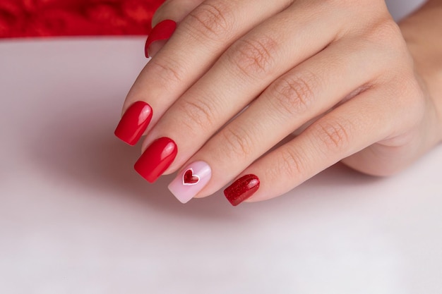 Foto mano femminile con unghie manicure rosse con disegno di cuore