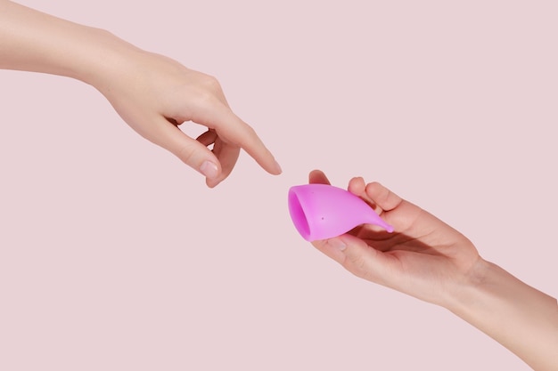 분홍색 배경에 재사용 가능한 생리컵이 있는 여성 손