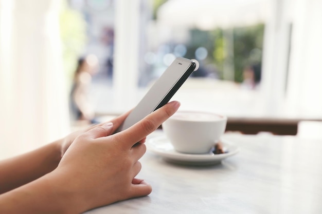 Female hand with smartphone trading stock online in coffee shop , business concept