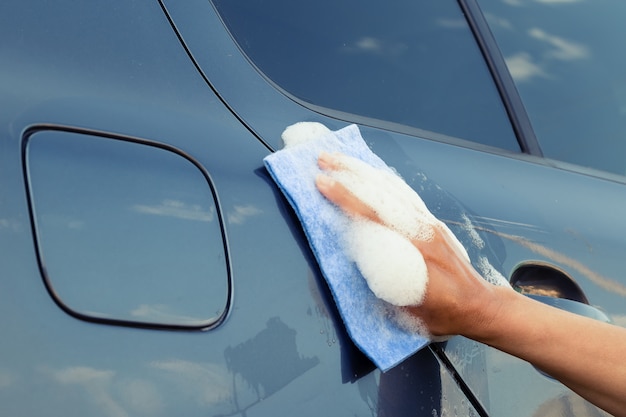 A female hand with sponge in soapy foam washes the car