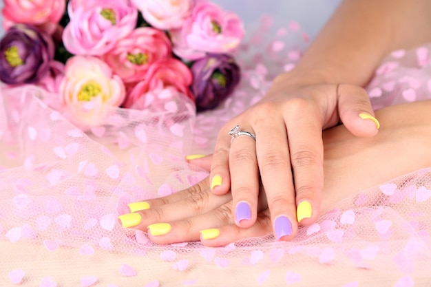 Female hand with stylish colorful nails on color fabric background