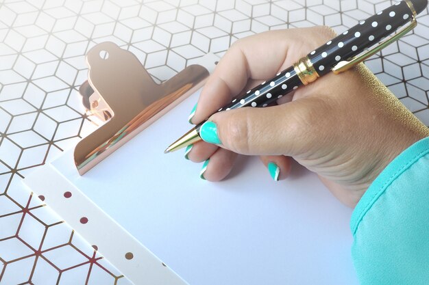 Female hand writes with a ballpoint pen on a clean sheet of paper on a clipboard. 