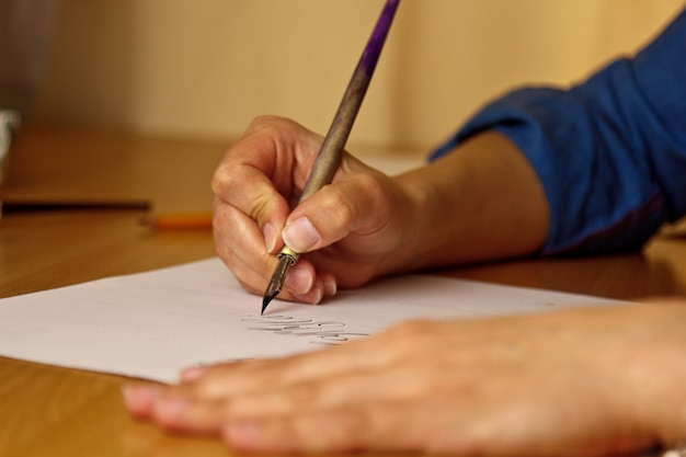 Photo female hand writes with the inky pen on a white paper sheet with stripes.