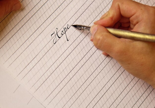 Female hand writes with the inky pen the word prize on a white paper sheet with stripes stationery on desk close up top view spelling lessons and caligraphy exercises Template layout background