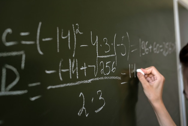 Photo female hand writing math formulas on the classboard, close-up