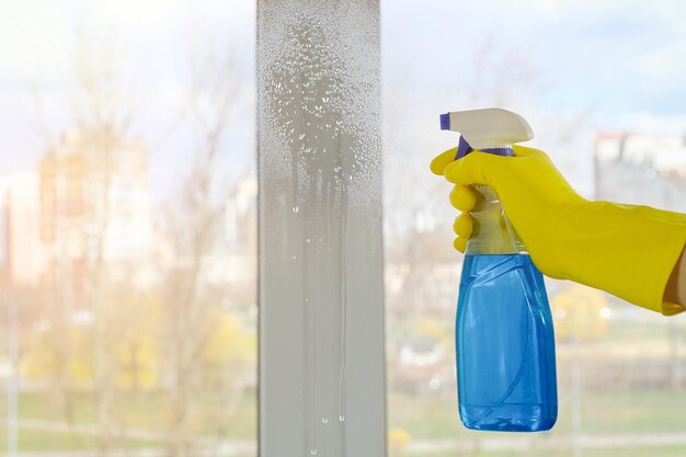 female hand in a yellow glove and detergent on the background of a window