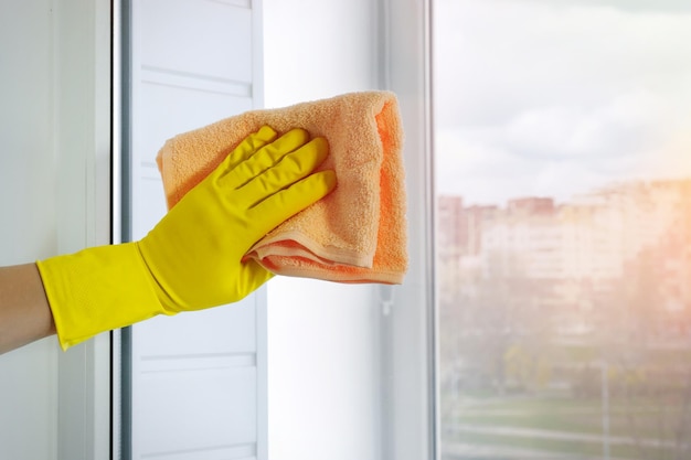 A female hand in a yellow glove with a rag rubs the window