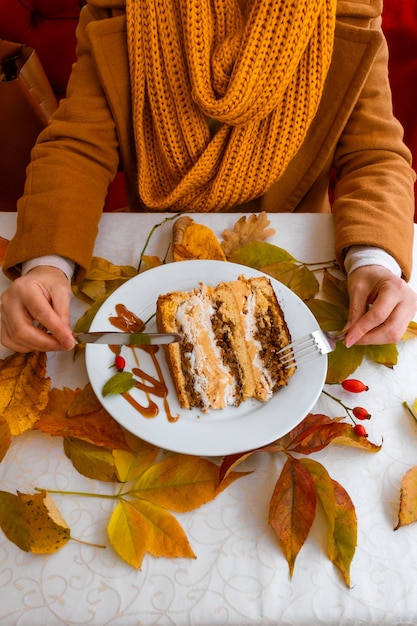 写真 女性の手と秋の落ち葉とテーブルの上のケーキとプレート