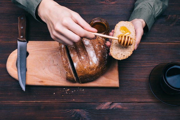 Female hands apply honey on the bread