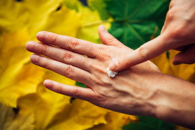 Mani femminili che applicano crema cosmetica idratante, primi piani