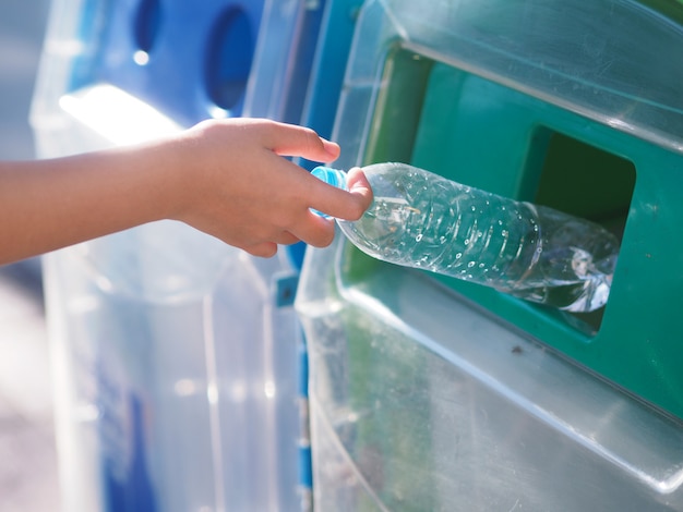 Female hands are dropping the plastic bottle  into the trash.       