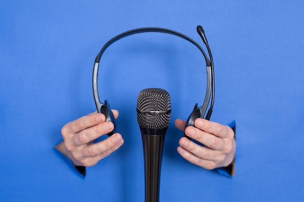 Female hands are holding a microphone and headphones on a blue background. Womens are inserted into a paper background. Place for an inscription.