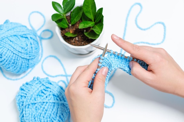 Female hands are knitting from yarn on white background top view