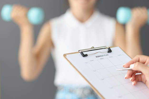 Female hands are writing down a workout plan, close-up, blurry. Fitness trainer control, exercises with dumbbells