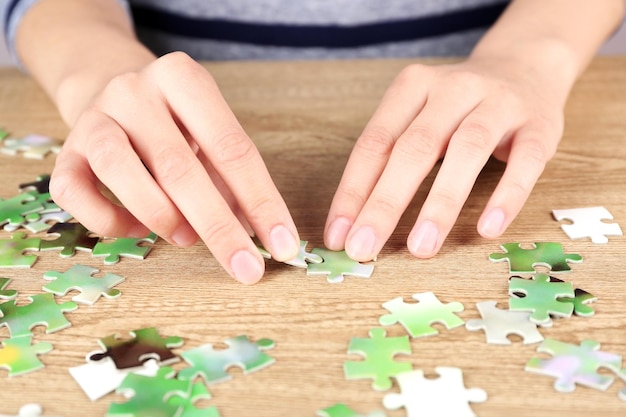 Foto mani femminili che assemblano un puzzle su un tavolo di legno in primo piano