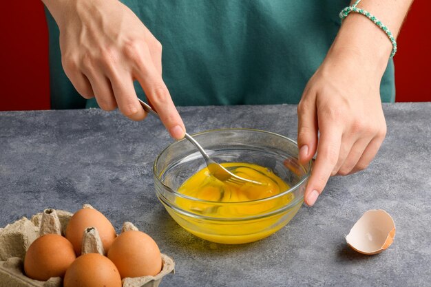 Foto le mani delle femmine battono le uova con la forchetta in una ciotola di vetro su un tavolo grigio della cucina