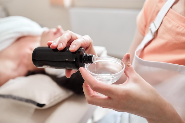 Female hands of a beautician with a bottle of phytic acid and a glass cup Cosmetic beauty procedure