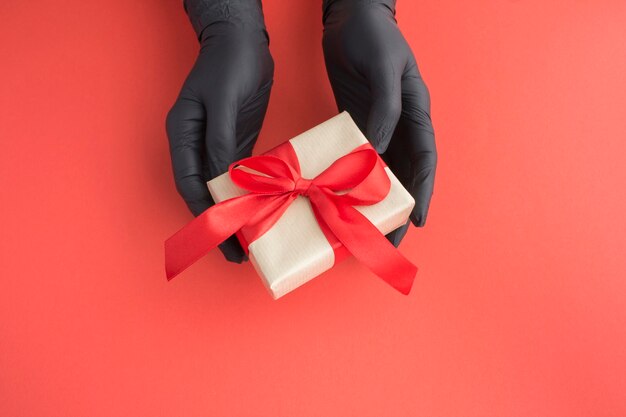 Female hands in a black gloves with gift on red