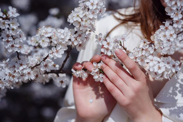 Female hands among blossom cherry tree brunch in spring garden, beauty, summer, emotion, expression and people concept.
